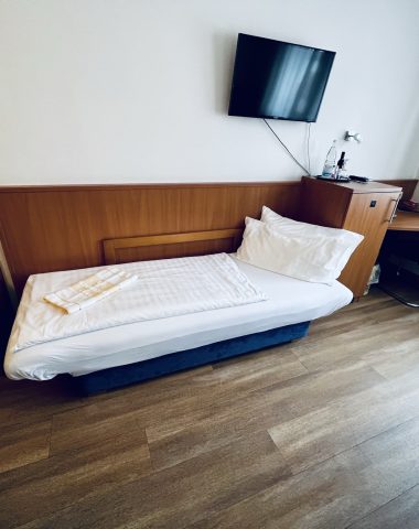 Modern hotel room with single bed and television.