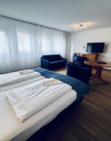 Modern hotel room with twin beds and seating area.