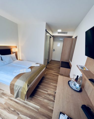 Modernes Hotelzimmer mit Doppelbett und Fernseher.