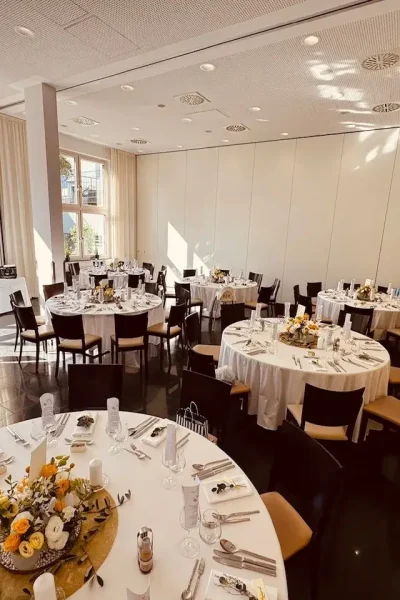 Saal im Goldenen Pflug Ludwigsburg mit mehreren festlich gedeckten runden Tischen und großen Fensterflächen.