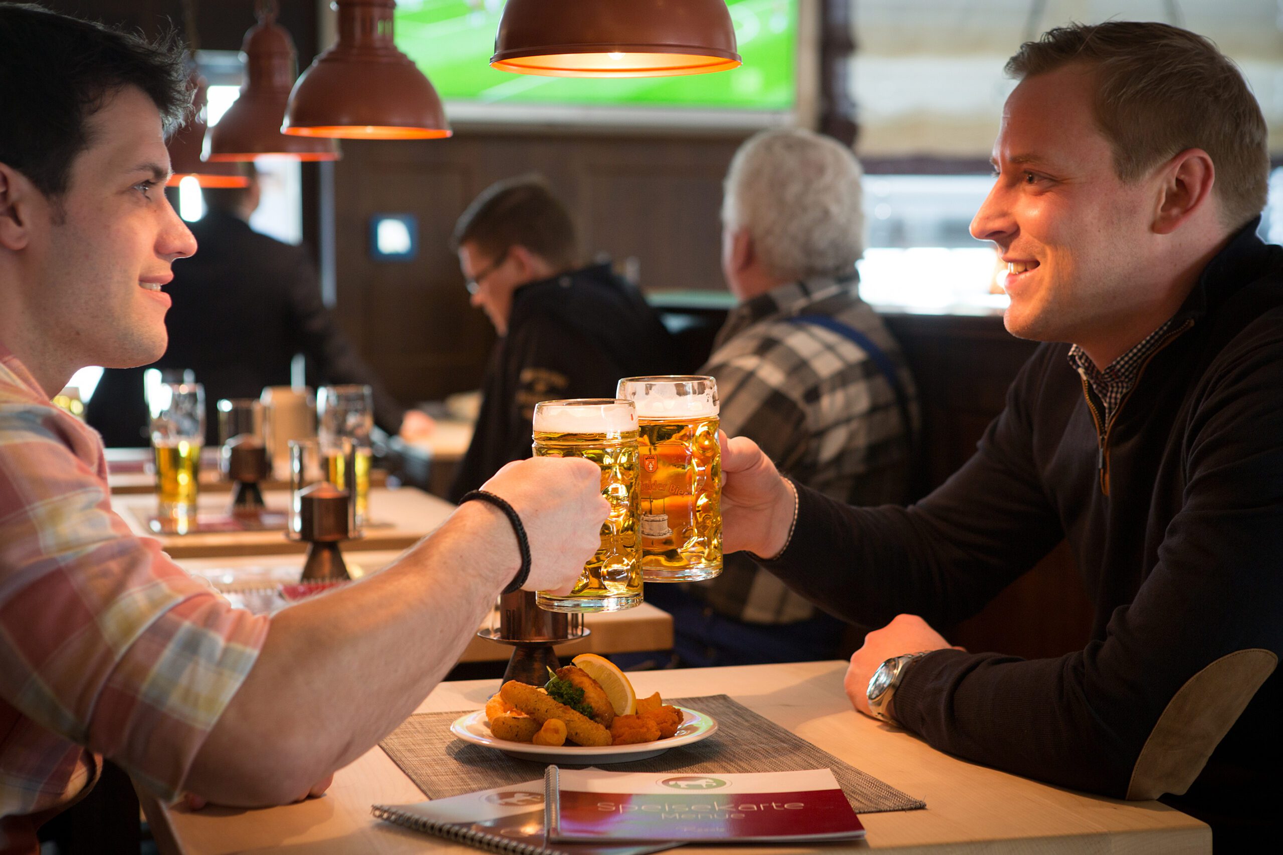 Zwei Männer prostend mit Bier in Kneipe.